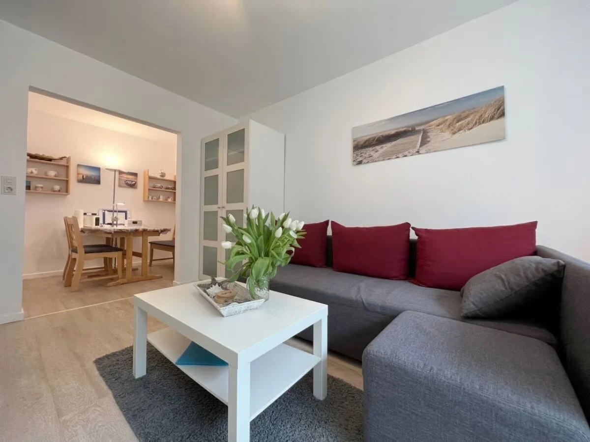 Wohnzimmer mit grauem Sofa, roten Kissen und weißem Couchtisch in unserer Ferienwohnung in St. Peter-Ording