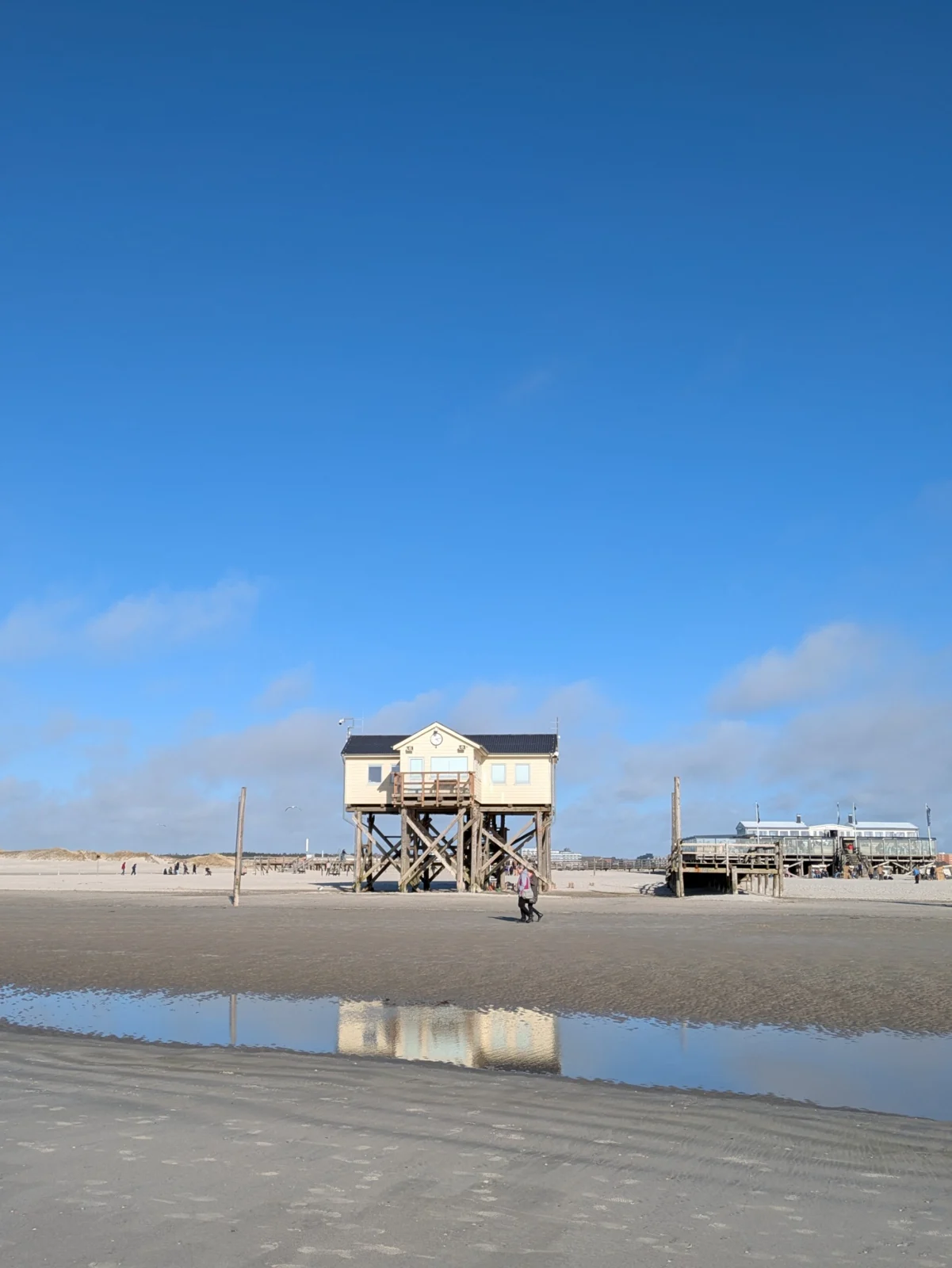Pfahlbau am Strand von St. Peter-Ording, der sich in einer flachen Wasserfläche im Sand spiegelt