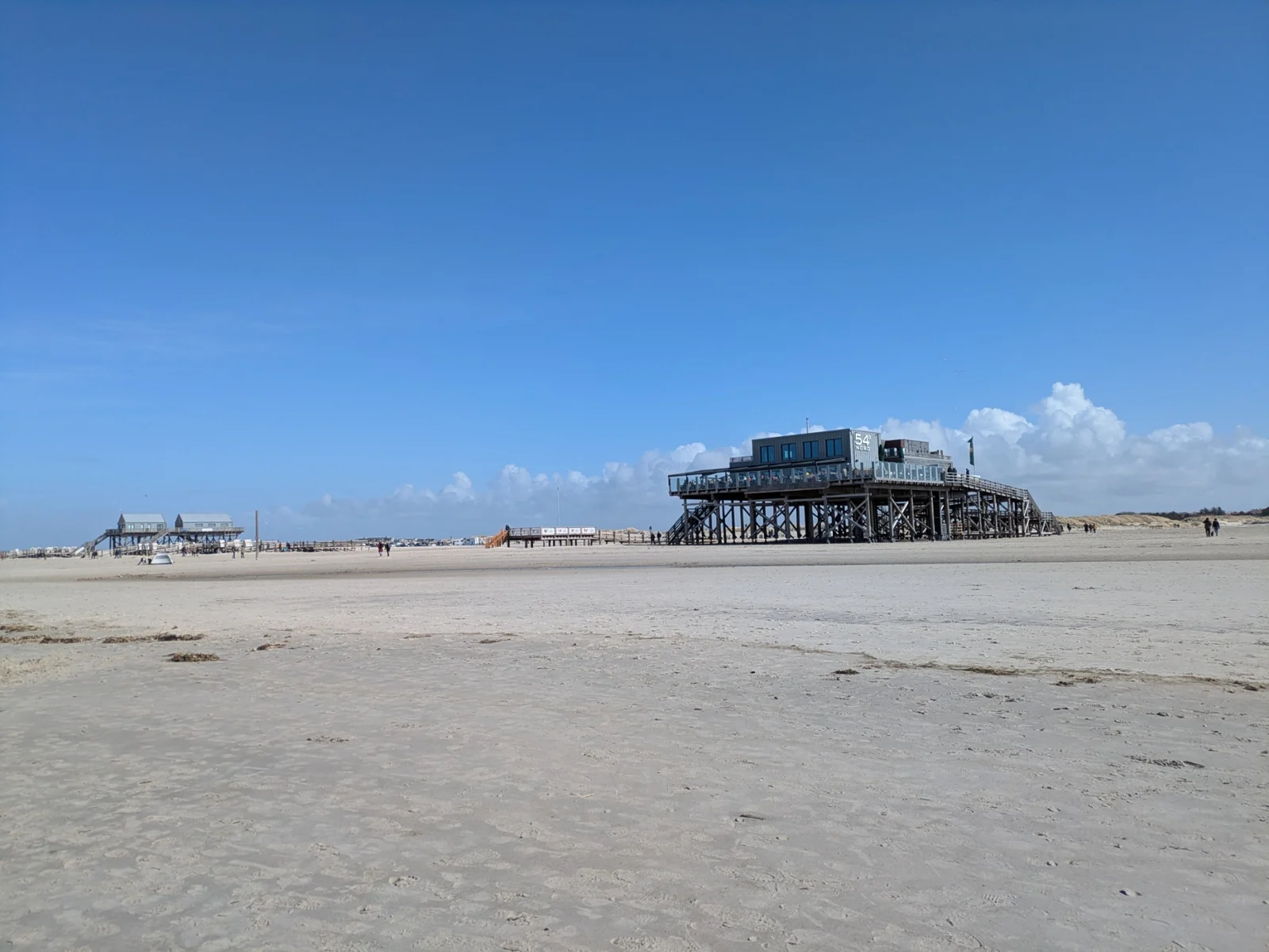 Pfahlbauten auf hohen Holzstützen am weiten Sandstrand von St. Peter-Ording unter blauem Himmel